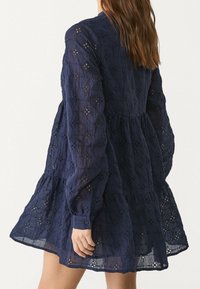 Robe en coton bleu marine à manches longues, avec un motif texturé et des poignets boutonnés. Comprend des découpes florales brodées et un ourlet évasé.