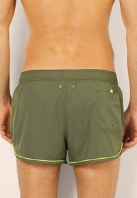 Gröna simshorts med dragsko i midjan, kontrasterande gula detaljer, två bakfickor med knapp och ett smidigt, lättviktigt tyg.