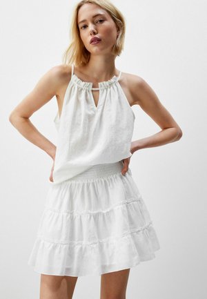 Robe blanche avec un col halter, un tissu froncé, un détail en goutte d'eau et une jupe à volants à plusieurs niveaux avec une taille smockée.