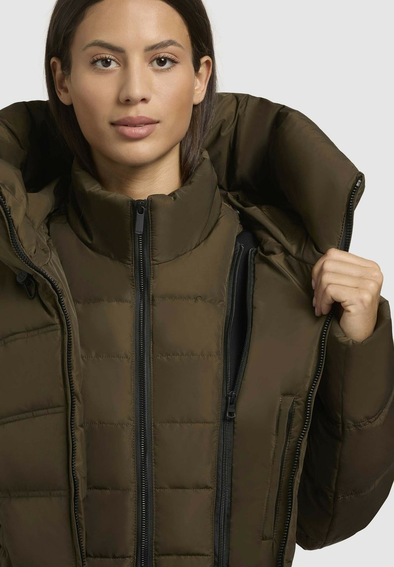 Grüne Pufferjacke mit hohem Kragen. Verfügt über eine gesteppten Struktur, Front-Reißverschlüsse und zwei Seitentaschen. Leichtes und figurbetontes Design.