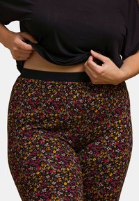 Leggings noirs avec un motif floral comprenant des fleurs roses, jaunes et crème. La taille est dotée d'un bandeau élastique noir. Tissu doux et extensible.