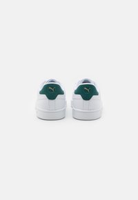 Sneaker bianche con un accento verde sul tallone, caratterizzate da un design testurizzato e un dettaglio del logo dorato sul retro. Suola piatta e chiusura con lacci.