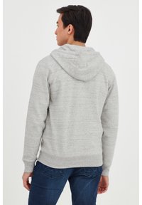 Grå hettegenser laget av teksturert stoff, med snor i hetten og ribbestrikkede mansjetter, kombinert med blå jeans. Enkel design uten mønstre.