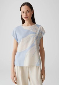 Hellblaues Blumenoberteil mit lockerer Passform, kurzen Ärmeln, einem runden Ausschnitt und einer glatten Textur, die einen großen Blumenprint in Creme zeigt.