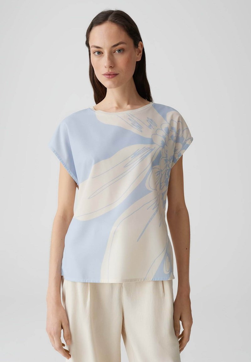Hellblaues Blumenoberteil mit lockerer Passform, kurzen Ärmeln, einem runden Ausschnitt und einer glatten Textur, die einen großen Blumenprint in Creme zeigt.