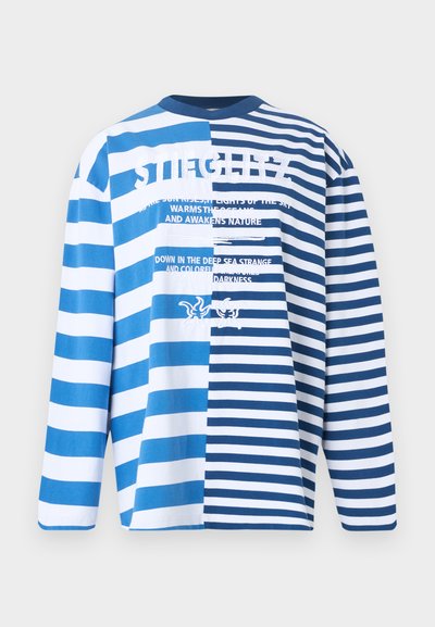 Πουκάμισο με μακριά μανίκια με εναλλασσόμενες φαρδιές και στενές μπλε και λευκές οριζόντιες ρίγες και λευκό κείμενο με φράσεις σχετικές με τη θάλασσα και γραφικά αστερία.