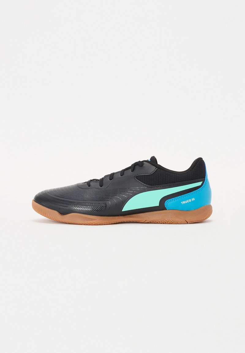 Zapatos de fútbol sala negros con una parte superior texturizada, detalles en azul claro y suela de goma. Presentan un diseño elegante y un talón reforzado.