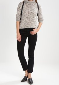 Pull à col roulé gris en maille avec motif texturé, associé à un jean noir ajusté et des ballerines noires à bout pointu.