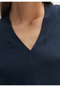 Námořnický pletený top s výstřihem do V, s hladkým povrchem a malými, nenápadnými stehy poblíž výstřihu.