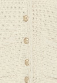 Cardigan en maille crème avec des bords tressés, quatre boutons décoratifs dorés et deux petites poches avant avec un bord tressé.