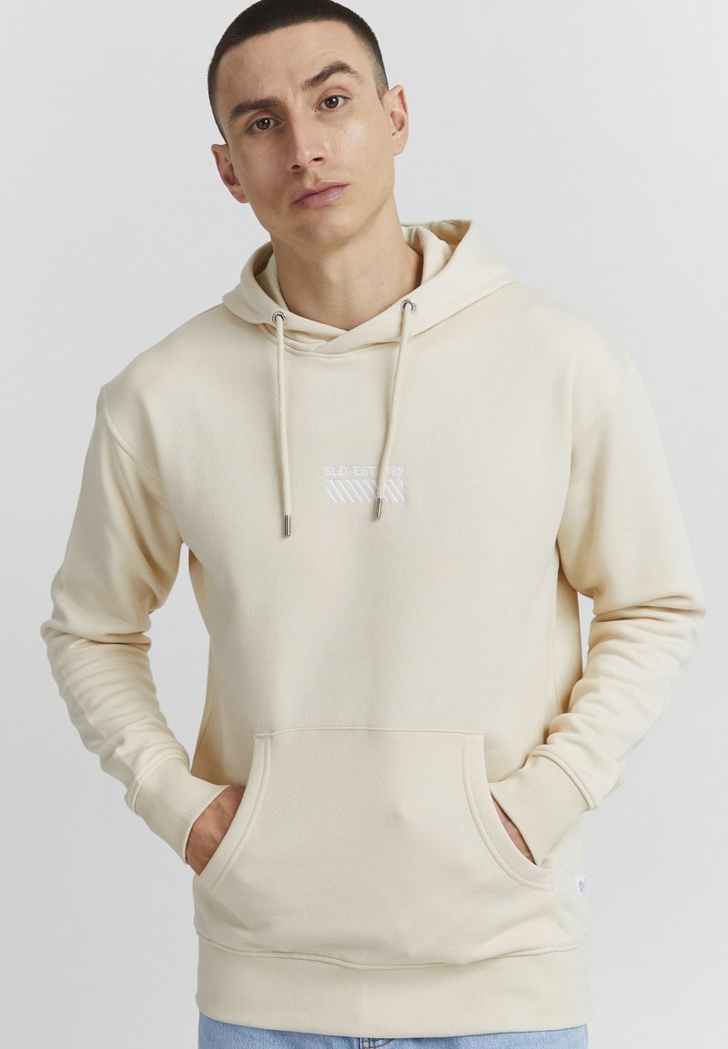 Felpa beige realizzata in tessuto morbido, dotata di tasca a marsupio, cappuccio con cordoncino e piccolo dettaglio logo bianco sul petto.