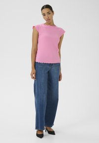 Rosa gerippter Oberteil mit gewellten Kanten, kombiniert mit weiteren blauen Denim-Jeans und schwarzen spitzen Absätzen. Einfache und moderne Designelemente.
