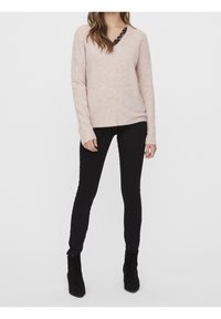 Pull rose clair en tricot avec un col en V et une bordure en dentelle noire, associé à un jean skinny noir et des bottines noires.