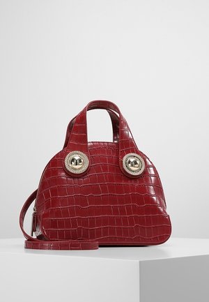 Sac à main en cuir rouge embossé façon crocodile avec deux poignées courtes, grands boutons décoratifs argentés et une bandoulière amovible, présenté sur une surface blanche.