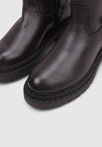 Botas de cuero marrón hasta el tobillo con un acabado texturizado, punta redonda y suela de goma gruesa. Los detalles de costura realzan el diseño y la durabilidad.