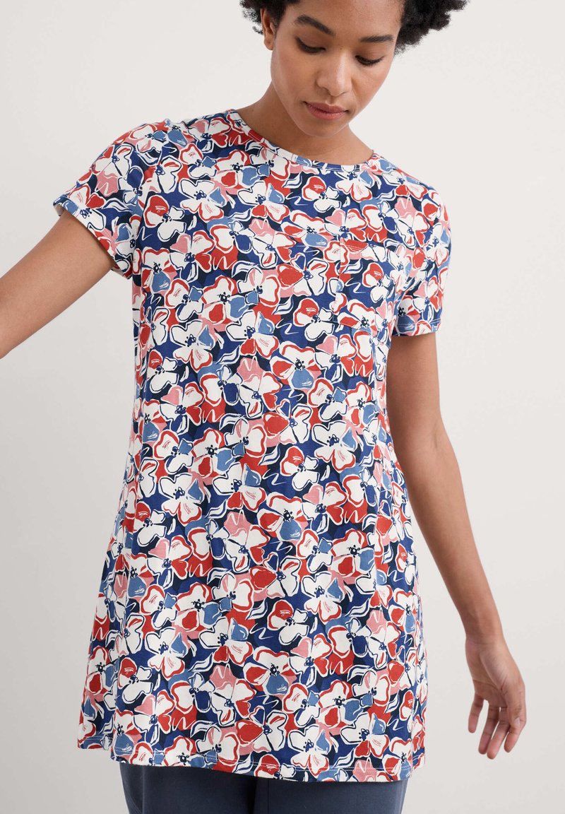 Túnica de manga corta con estampado floral que presenta una mezcla de flores rojas, rosas y azules sobre un fondo blanco. Fabricada con un tejido ligero y suave.