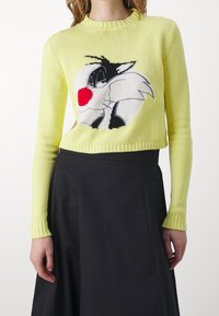 Jasnożółty sweter dziergany o krótkim kroju, z czarno-białą postacią z kreskówki wplecioną na środku. Ściągacze na mankietach.