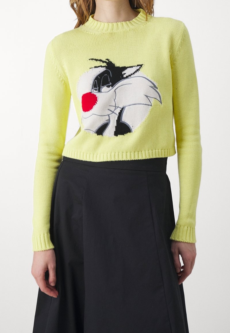 Jasnożółty sweter dziergany o krótkim kroju, z czarno-białą postacią z kreskówki wplecioną na środku. Ściągacze na mankietach.