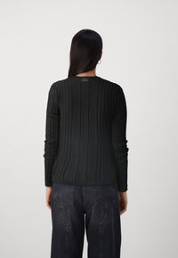 Schwarzes, geripptes Langarmoberteil mit rundem Ausschnitt. Es weist ein strukturiertes Muster auf und wird mit dunklen, weit geschnittenen Jeans kombiniert.