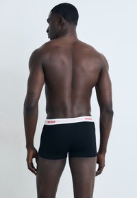 Schwarze Boxershorts mit einem weiß-roten HUGO-Logo-Bündchen, figurnaher Passform und glattem Baumwollmaterial, von hinten betrachtet.