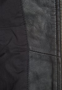 Black jacket featuring a mix of textured leather and smooth fabric, with visible stitching and a metallic zipper along the side.