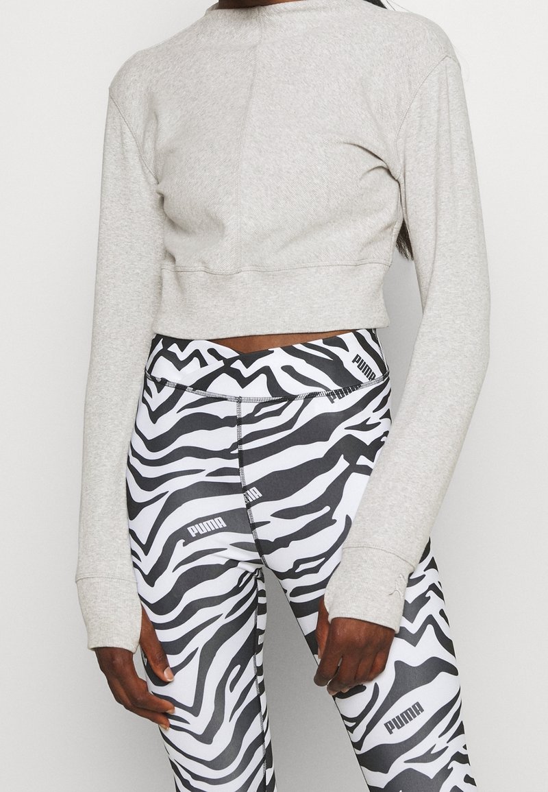 Personne portant un crop top gris clair à manches longues et des leggings Puma à rayures zèbre noir et blanc avec logo visible.