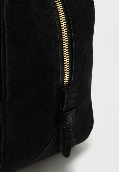 Μαύρο σουέντ μποτάκι με χρυσό φερμουάρ και μαύρο δερμάτινο λουράκι, εμφανιζόμενο σε κοντινή λήψη σε λευκό φόντο.