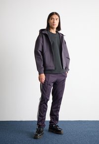 Dark purple zip-up jacket, black t-shirt, matching jogger pants with white side stripes, and black platform shoes. Minimalist design, smooth texture.