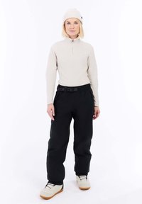 Lichtbeige ritsfleece-top en zwarte, losvallende broeken, gecombineerd met crèmekleurige schoenen met een tan zool.