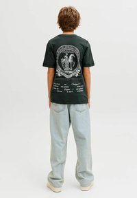 Juoda medvilninė marškinėliai su dideliu baltu grafiniu spauda ant nugaros, derinami su šviesiai mėlynomis laisvomis džinsinėmis kelnių.