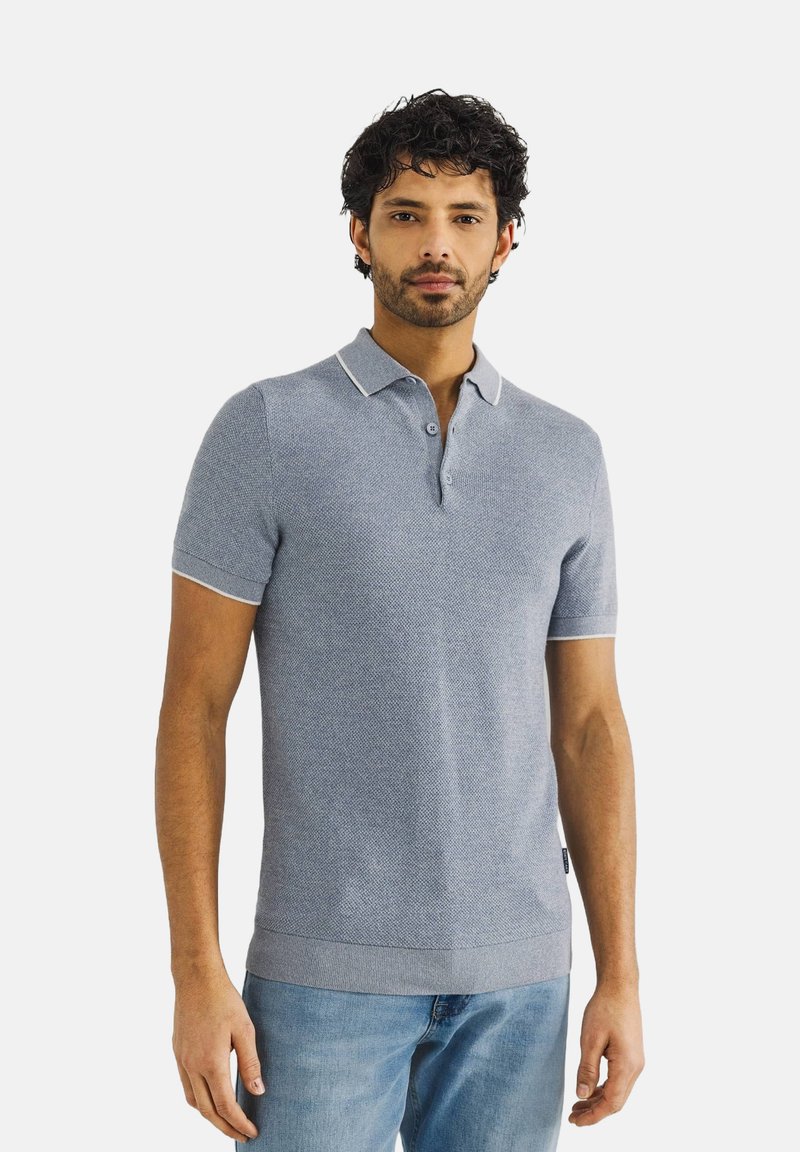 Lichtblauw polo shirt met korte mouwen, een gestructureerd patroon, geribbeld kraagje en witte rand. Gecombineerd met blauwe jeans met een getailleerd ontwerp.
