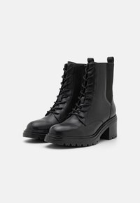 Botas de tobillo de cuero negro con un acabado texturizado, cordones en la parte delantera, paneles laterales elásticos y un tacón cuadrado grueso. Suela resistente para tracción.