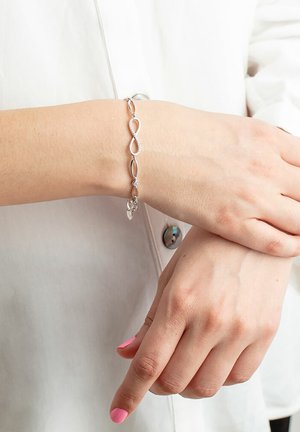 Silver bracelet featuring interconnected infinity and oval links, adorned with small accents and a delicate charm. Textured and polished finish.