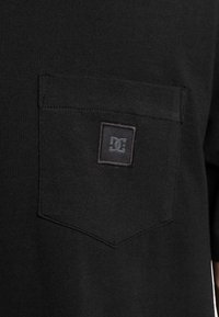 Černé tričko s krátkým rukávem s náprsní kapsou a černým logem DC. Vyrobeno z hladké tkaniny s jednoduchým, klasickým designem.