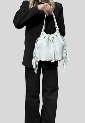 Persona con abbigliamento nero che tiene una borsa a secchiello in pelle bianca con chiusura a cordoncino e dettagli a frangia sui lati.