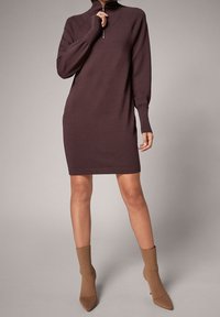 Ciemnobordowa dzianinowa sukienka z kołnierzem na zamek, długimi rękawami i dopasowaną sylwetką. Ma gładką fakturę i sięga do kolan.