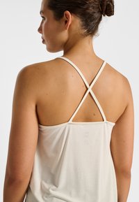 Slightly loose, light beige tank top with thin, crisscross straps at the back and a smooth texture, suitable for casual wear.