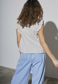 Lysstribet bluse med flæser ved skuldrene, sat sammen med vidde denim bukser. Glat stof, lyse farver og afslappet pasform.