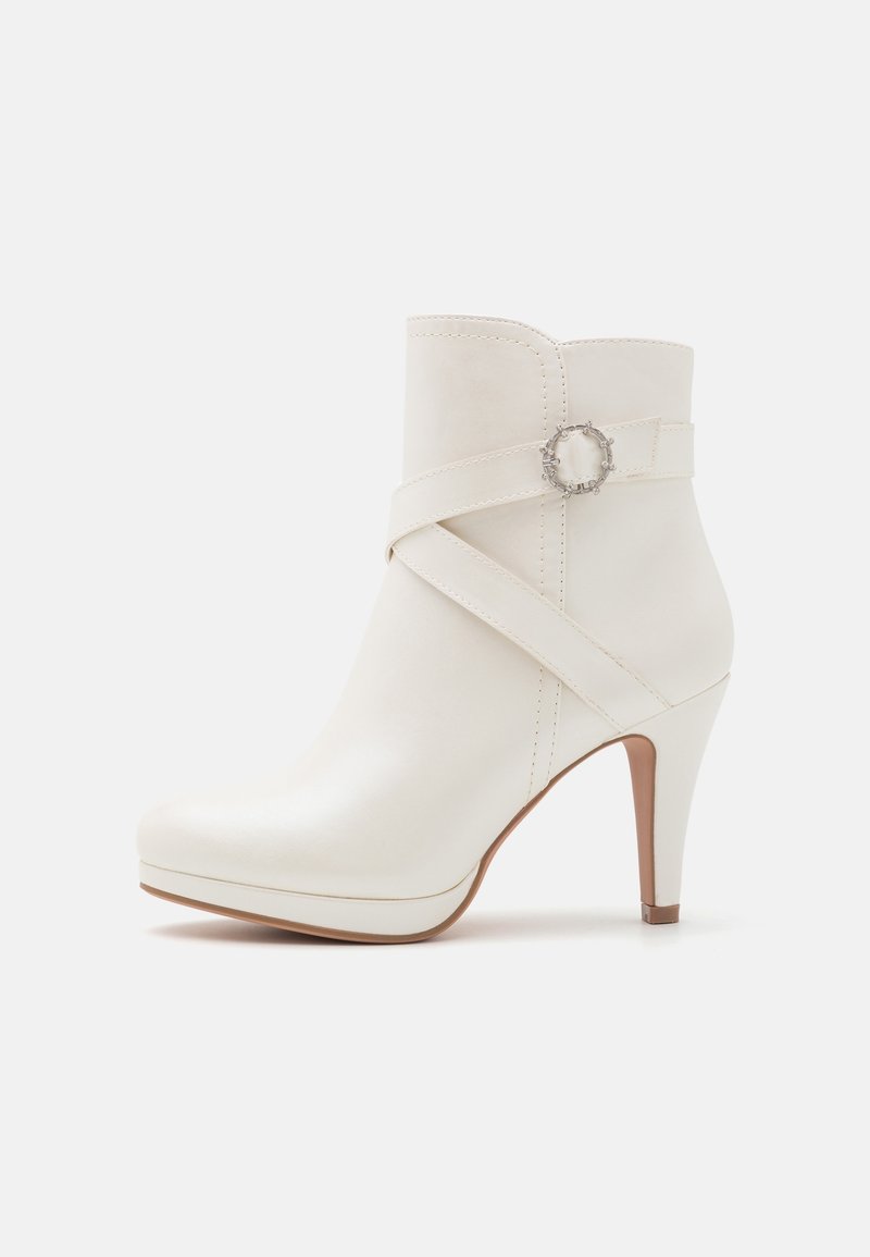 Vit ankelboot i slät läder, med spetsig tås, hög stilettklack och ett band med en cirkulär silverdetalj.