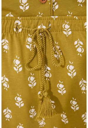 Tissu vert olive avec un motif floral blanc, présentant une taille à cordon de serrage avec un détail de pompon et une fermeture à bouton en bois en haut.