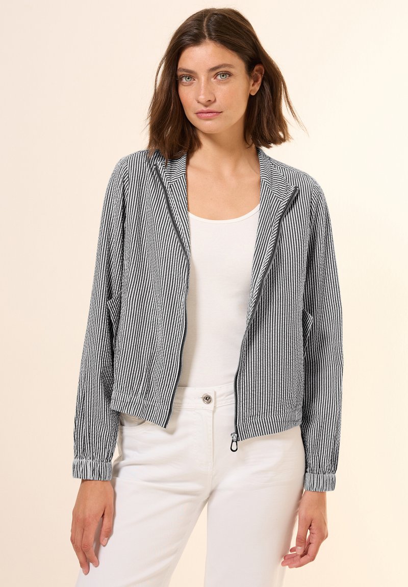 Veste cropped rayée, marine et blanche, en tissu léger, fermeture zippée, poignets légèrement élastiqués, dotée de poches latérales et d'un col.