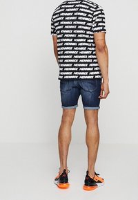 Black and white graphic t-shirt with “MENACE” text, paired with blue denim shorts. The outfit includes black and orange sneakers.