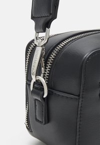 Black leather bag with silver zipper and hardware details. Features a wide zipper closure and a sturdy strap attachment.