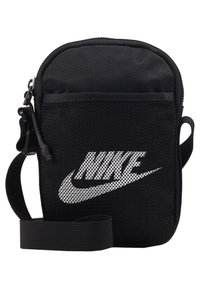 Černá crossbody taška Nike s bílým logem, síťovanou přední kapsou, zapínáním na zip a nastavitelným ramenním popruhem.