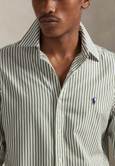 Πουκάμισο με ρίγες σε ανοιχτό πράσινο και λευκό, με κλασικό γιακά, κούμπωμα με κουμπιά στο μπροστινό μέρος και μπλε κεντημένο λογότυπο στο στήθος. Υφασμα από μείγμα βαμβακιού.