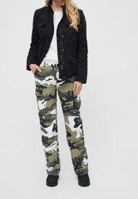 Giacca nera di cotone con due tasche frontali, abbinata a pantaloni cargo mimetici verdi e bianchi con multiple tasche e una vestibilità comoda.