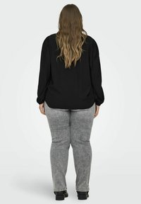 Blusa nera a maniche lunghe in tessuto testurizzato, vestibilità ampia, con leggere pieghe sulle spalle. Abbinata a pantaloni in denim grigio chiaro e calzature nere.