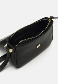 Musta nahkalaukku vetoketjulla, kultaisilla yksityiskohdilla, kahdella sisäosastolla ja irrotettavalla hihnalla. Sileä pinta ja minimalistinen muotoilu.