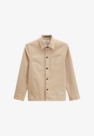 Beige langärmliges Hemd mit Knöpfen, Kragen, zwei Brusttaschen, schwarzen Knöpfen und einem kleinen weißen Etikett nahe dem Saum.