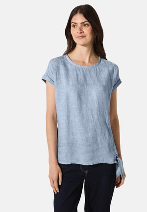 Blusa di lino azzurro chiaro con maniche corte arrotolate, scollatura rotonda e dettaglio a fiocco laterale. Il materiale sembra testurizzato e traspirante.